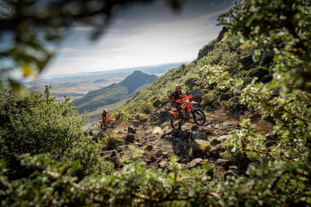 Two motorcyclists ride 2025 KTM EXC RANGE bikes through a wooded area